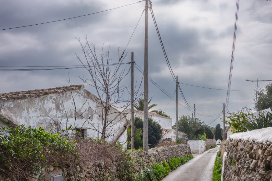 Landweg bei Maó mit weiß getünchten Häusern und Trockenmauern unter bewölktem Himmel